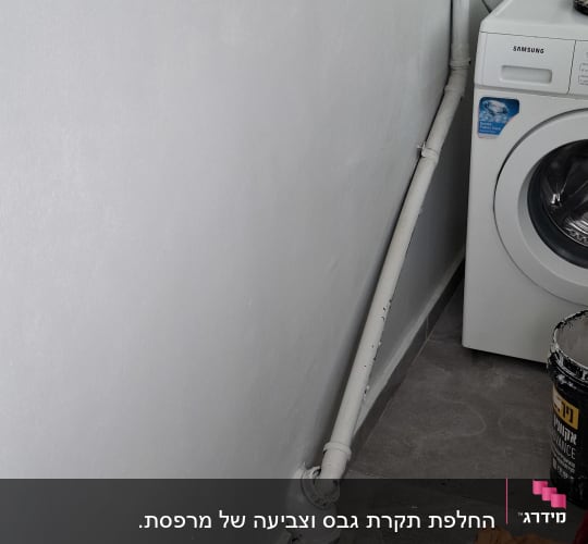 קיר צבוע ליד מכונת כביסה עם צינור ודלי צבע